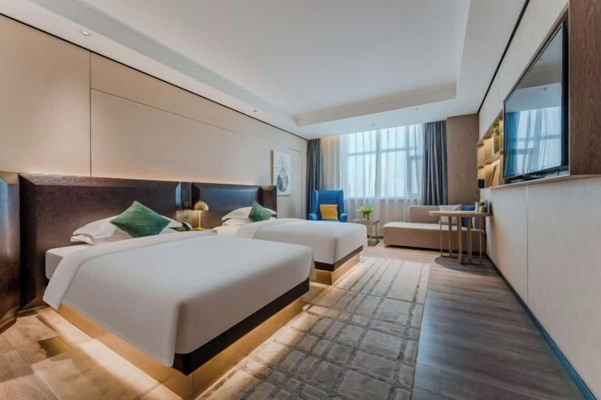 A hotel room with two beds, a desk, a chair, and a large window.