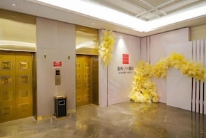 A hotel lobby with a reception desk, a trash bin, and a wall-mounted elevator control panel. - Echarm Plus Hotel Taiyuan Wanda Plaza Railway Station Store (Taiyuan)