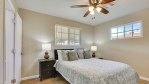 A bedroom with a bed, nightstands, lamps, a ceiling fan, and a window.