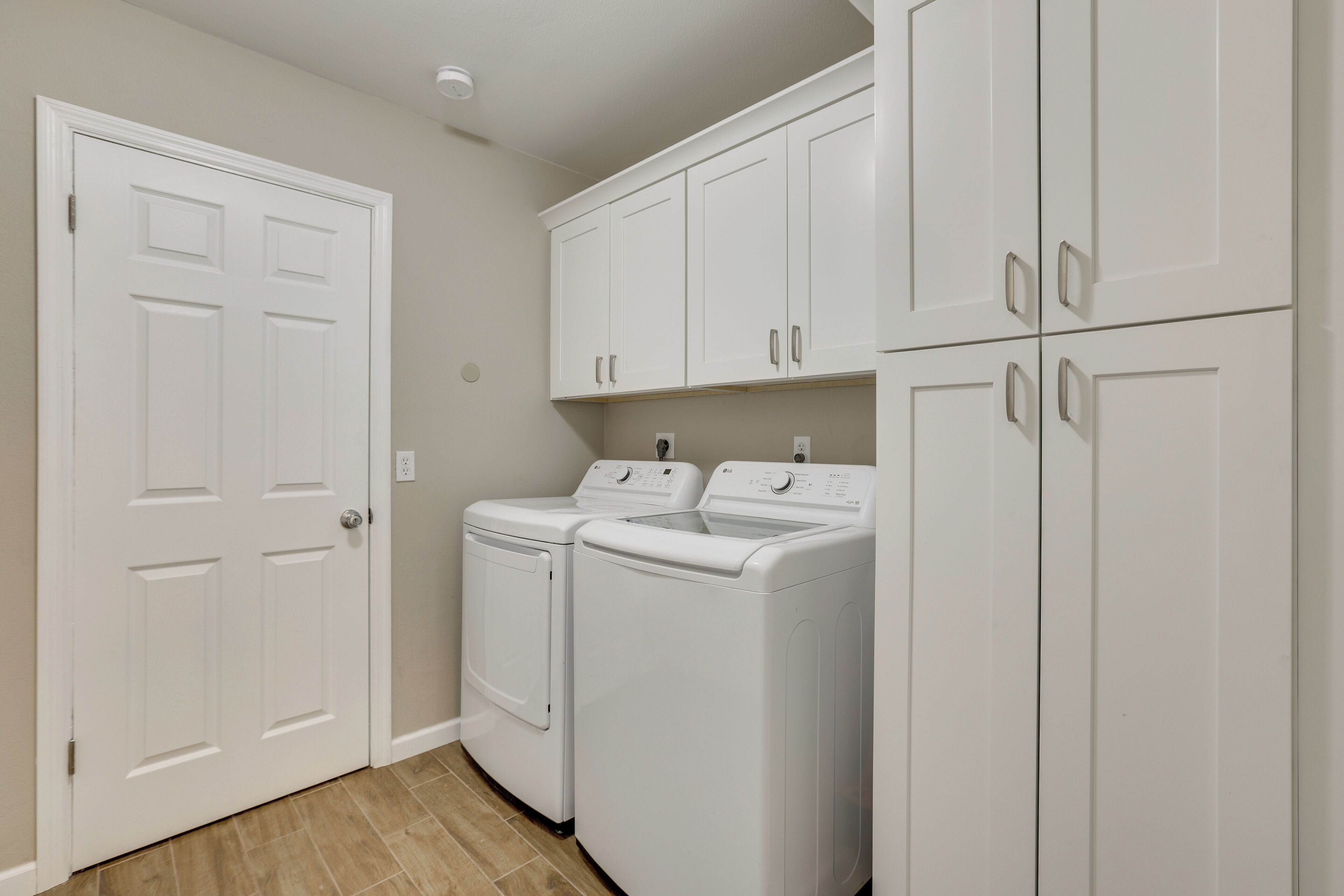 A laundry room with two front-loading washing machines, a white door, and white cabinetry.