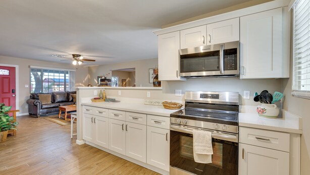 A modern kitchen with white cabinets, stainless steel appliances, and a wooden floor.