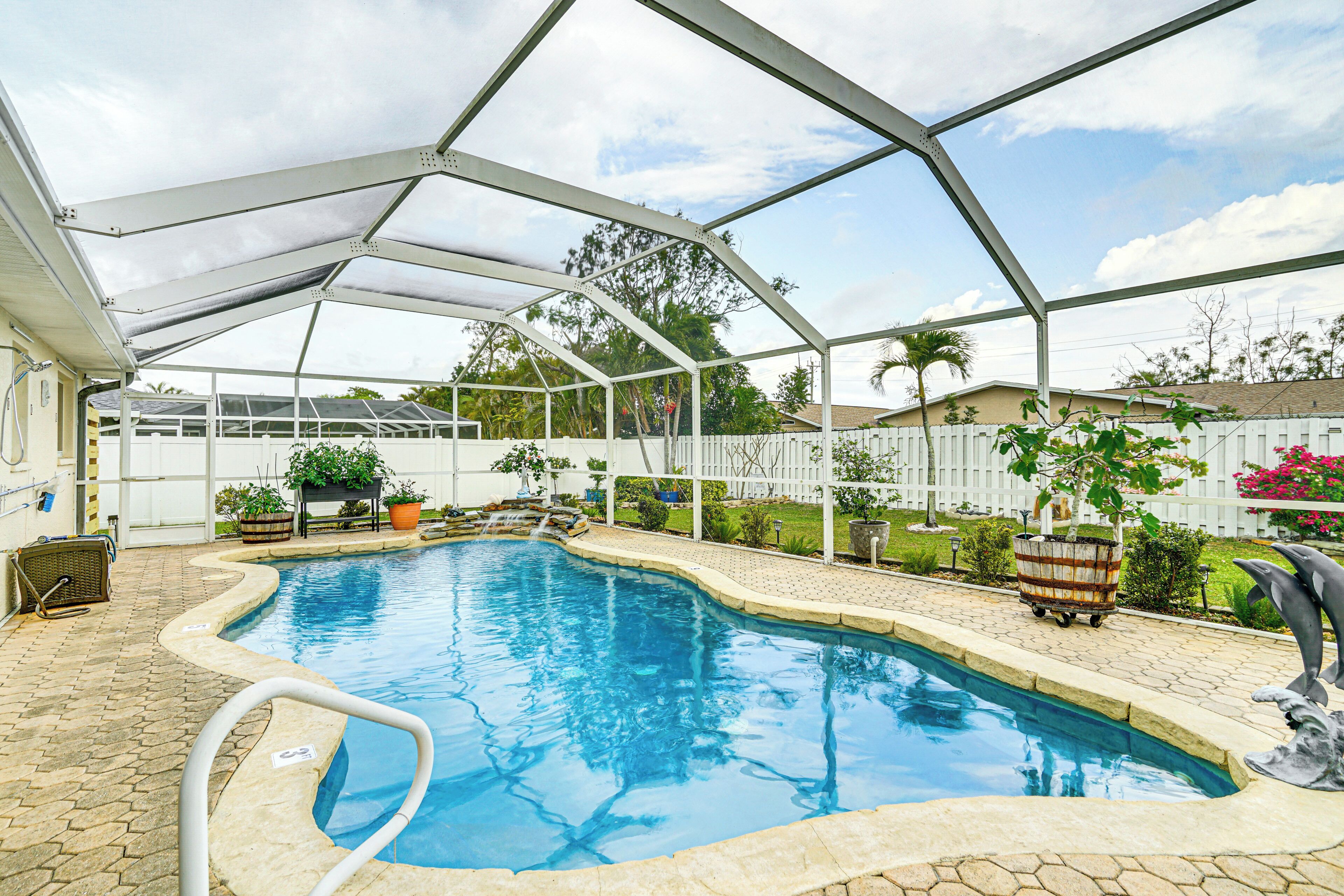 A covered swimming pool with a white fence, potted plants, and a dolphin statue.