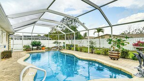A covered swimming pool with a white fence, potted plants, and a dolphin statue.