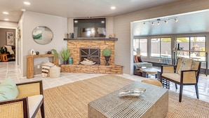 A spacious living room with a stone fireplace, a ceiling fan, and large windows. - Walk to Scottsdale Stadium: Remodeled Home! (Scottsdale)