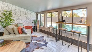 A modern living room with a pool view, a cowhide rug, and a wall with floral line drawings. - Walk to Scottsdale Stadium: Remodeled Home! (Scottsdale)