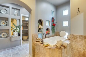 A modern bathroom with a large bathtub, a vanity with a sink, and shelves with decorative items. - Walk to Scottsdale Stadium: Remodeled Home! (Scottsdale)