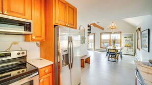 A modern kitchen with wooden cabinets, stainless steel appliances, and a dining area with a chandelier. - 2 Mi to Stone Harbor Beach: Lovely Bayfront Home (Cape May Court House)