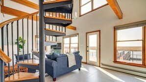 A spacious living area with a blue sofa, wooden staircase, and large windows offering a view of the outdoors. - 2 Mi to Stone Harbor Beach: Lovely Bayfront Home (Cape May Court House)