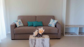 A living room with a beige sofa, teal and blue patterned pillows, and a white wooden coffee table with a floral arrangement. - HOTEL ACQUAMARINA (Portoferraio)