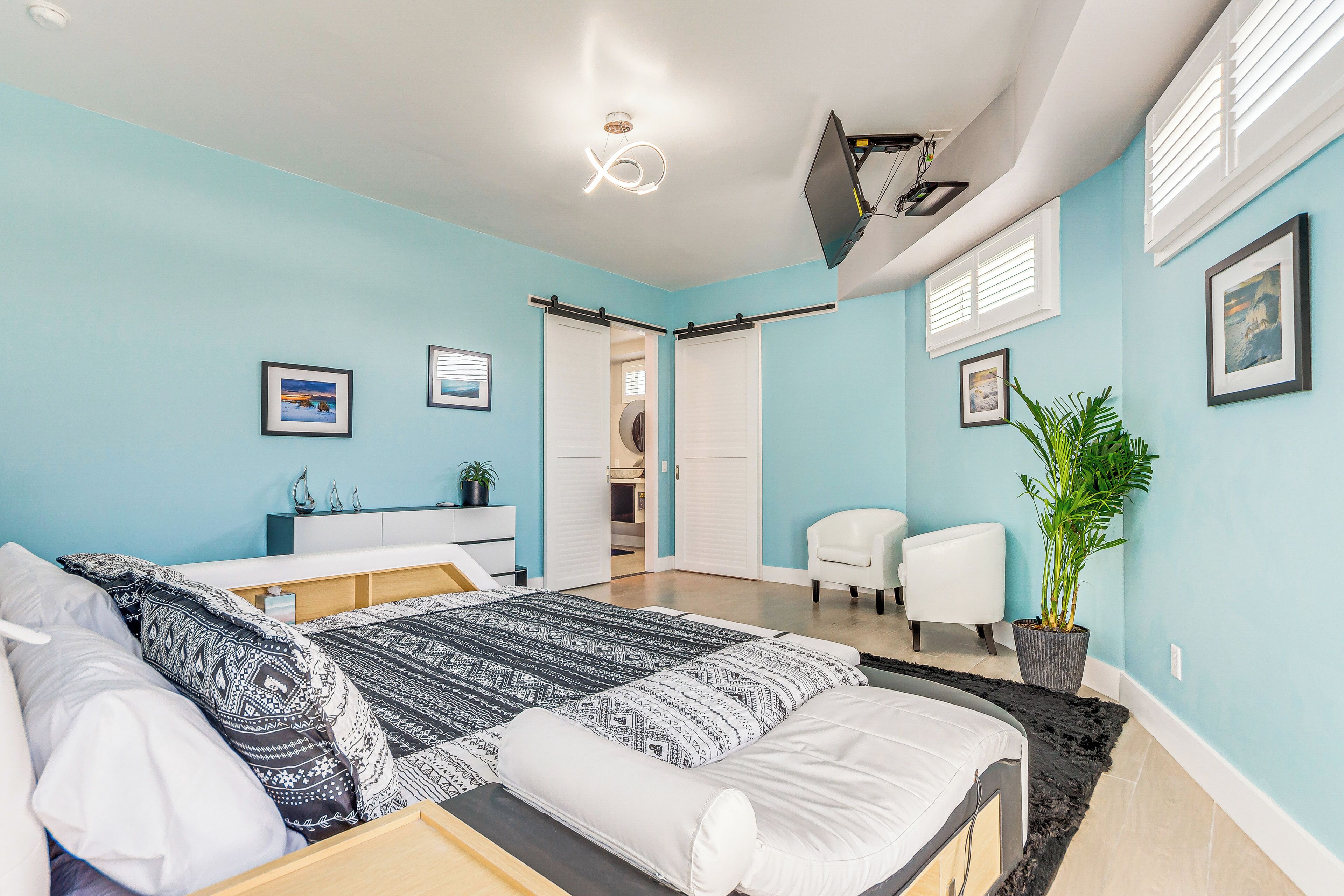 A bedroom with a bed, bedside tables, a desk, a chair, a potted plant, and a TV.