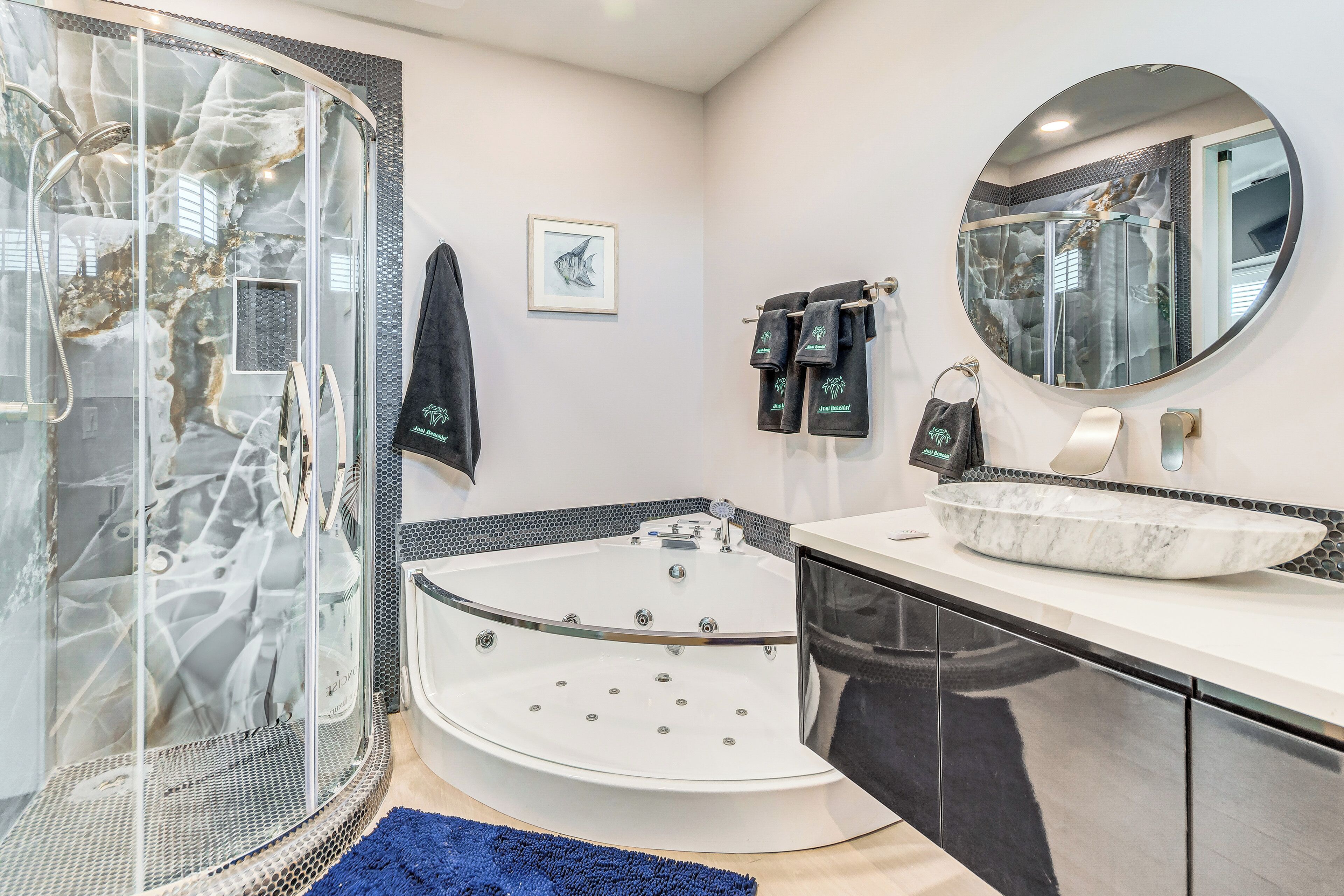 Un baño moderno con ducha envuelta en cristal, una bañera grande independiente y un espejo redondo sobre el lavabo.