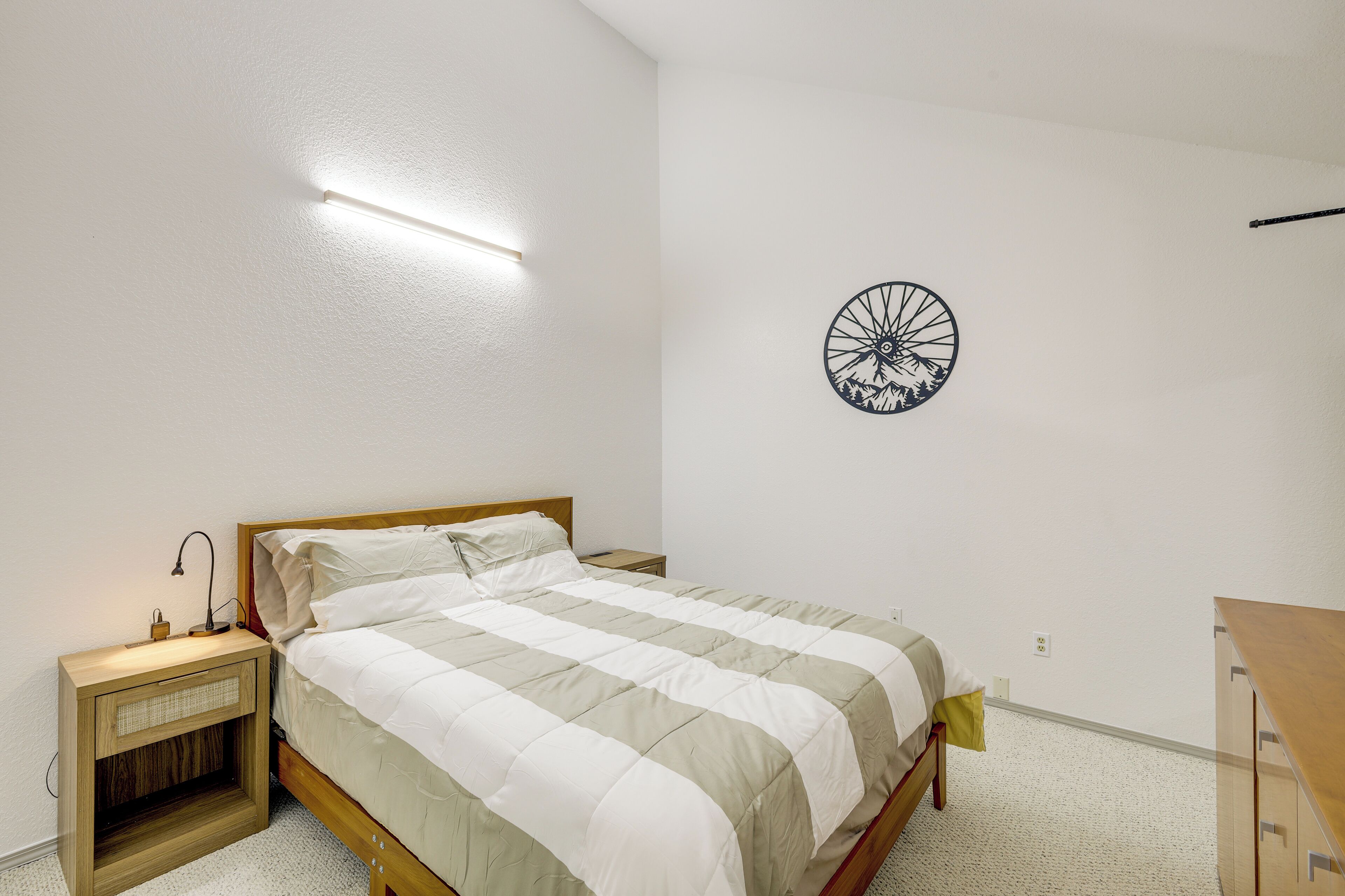 A bedroom with a bed, bedside table, lamp, and a wall decoration.