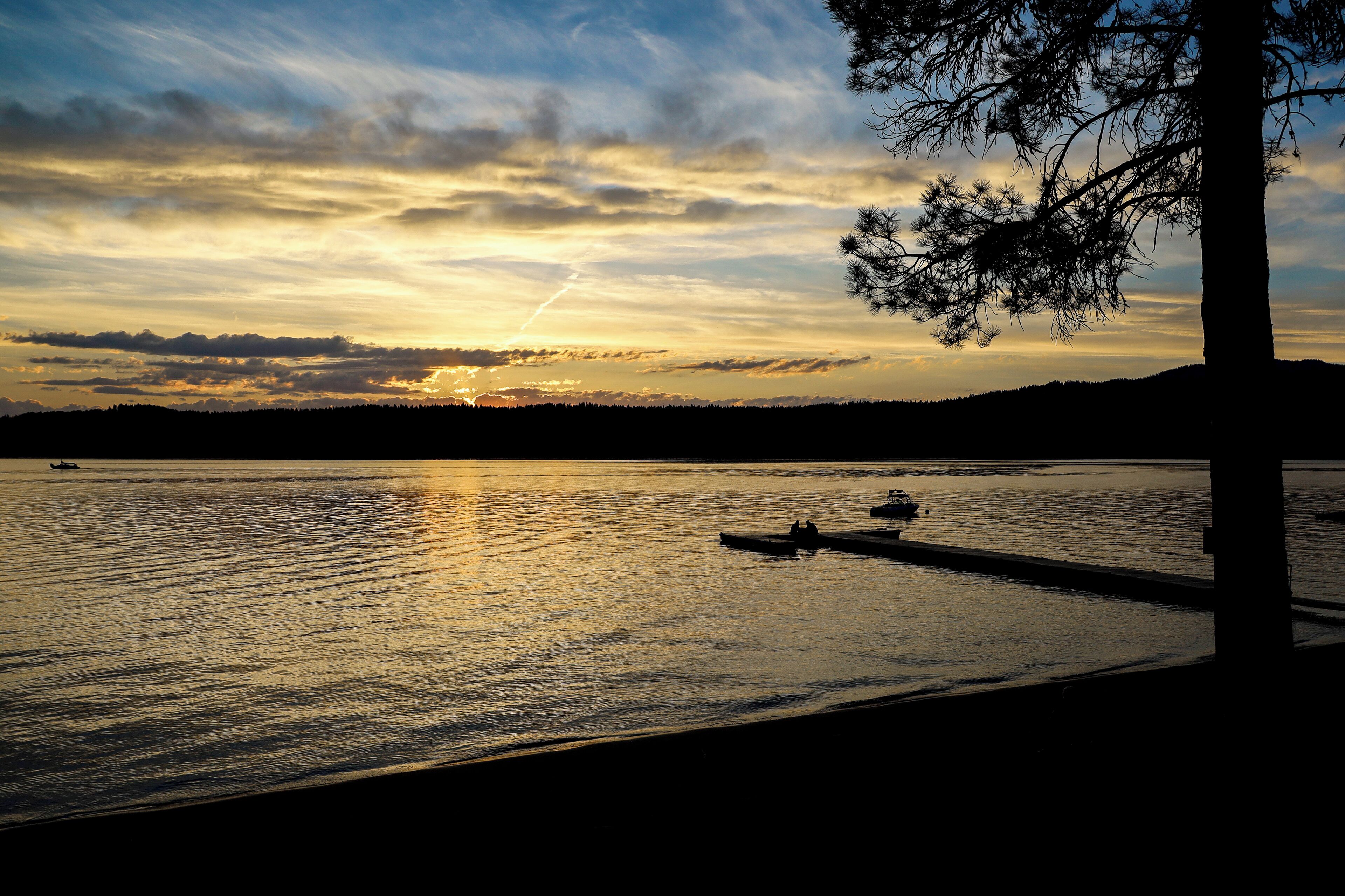 A sunset over a calm lake with boats, a dock, and a tree silhouette.