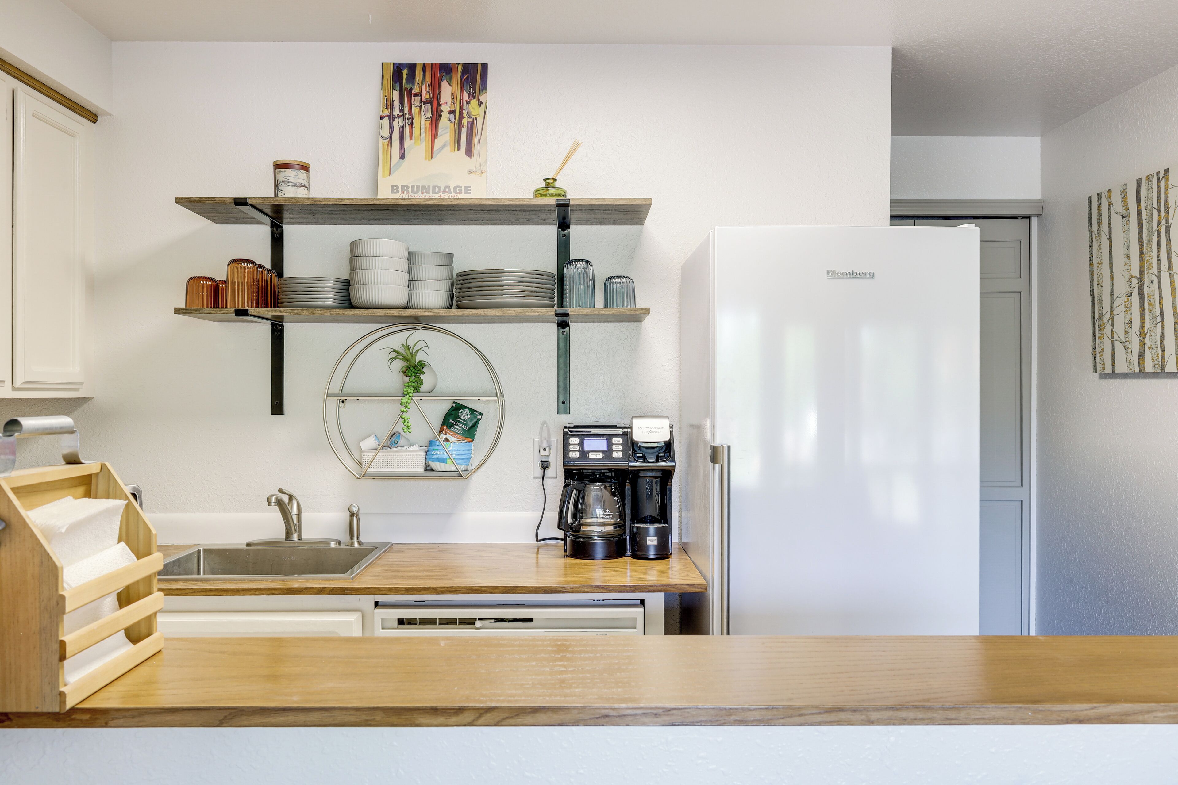 A modern kitchen with a white refrigerator, a coffee maker, and shelves with dishes and jars.