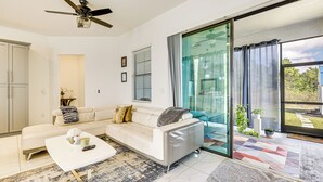 Un salon moderne avec un canapé blanc, une table basse et une porte vitrée donnant sur un balcon.