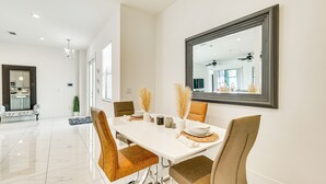 Un espace repas moderne avec une table blanche, des chaises marron et un grand miroir au mur.