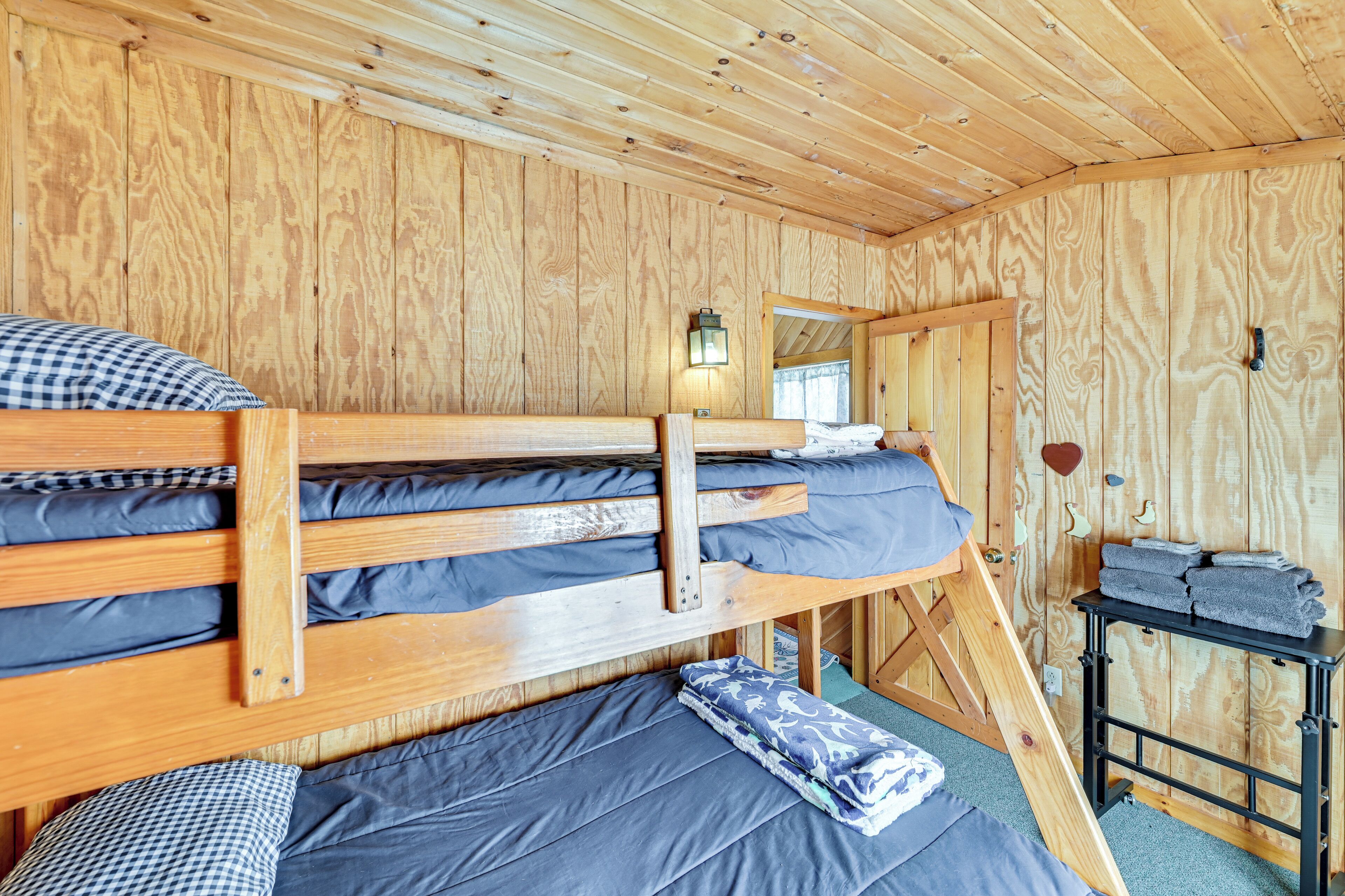 A wooden cabin room with bunk beds, a small table with towels, and a wall-mounted light fixture.