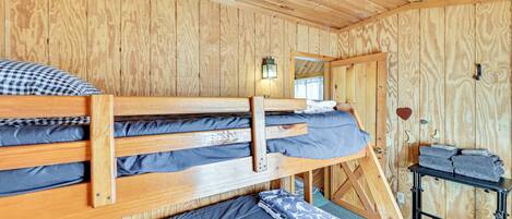 A wooden cabin room with bunk beds, a small table with towels, and a wall-mounted light fixture.