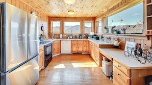 Une cuisine moderne avec des meubles en bois, des appareils électroménagers en acier inoxydable et de grandes fenêtres offrant une vue sur les montagnes.