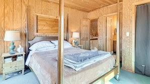 Une chambre à coucher dans une cabane en bois, avec un lit à baldaquin, deux tables de chevet avec des lampes et une porte donnant sur une autre pièce.