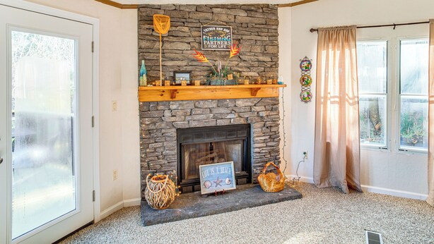 A cozy room with a stone fireplace, a wooden mantel, and a view of the outdoors through a large window. - Fish On-site: Lake Murray Family Home (Prosperity)