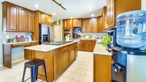 Una cocina moderna con armarios de madera, electrodomésticos de acero inoxidable, dispensador de agua y un taburete de bar.