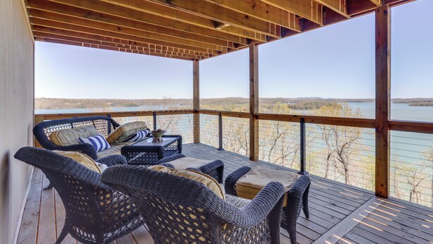 Un espacio de estar al aire libre techado con mobiliario de mimbre y vistas a un lago.