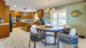 Una cocina moderna con armarios de madera, una isla central y un comedor con sillas de mimbre.