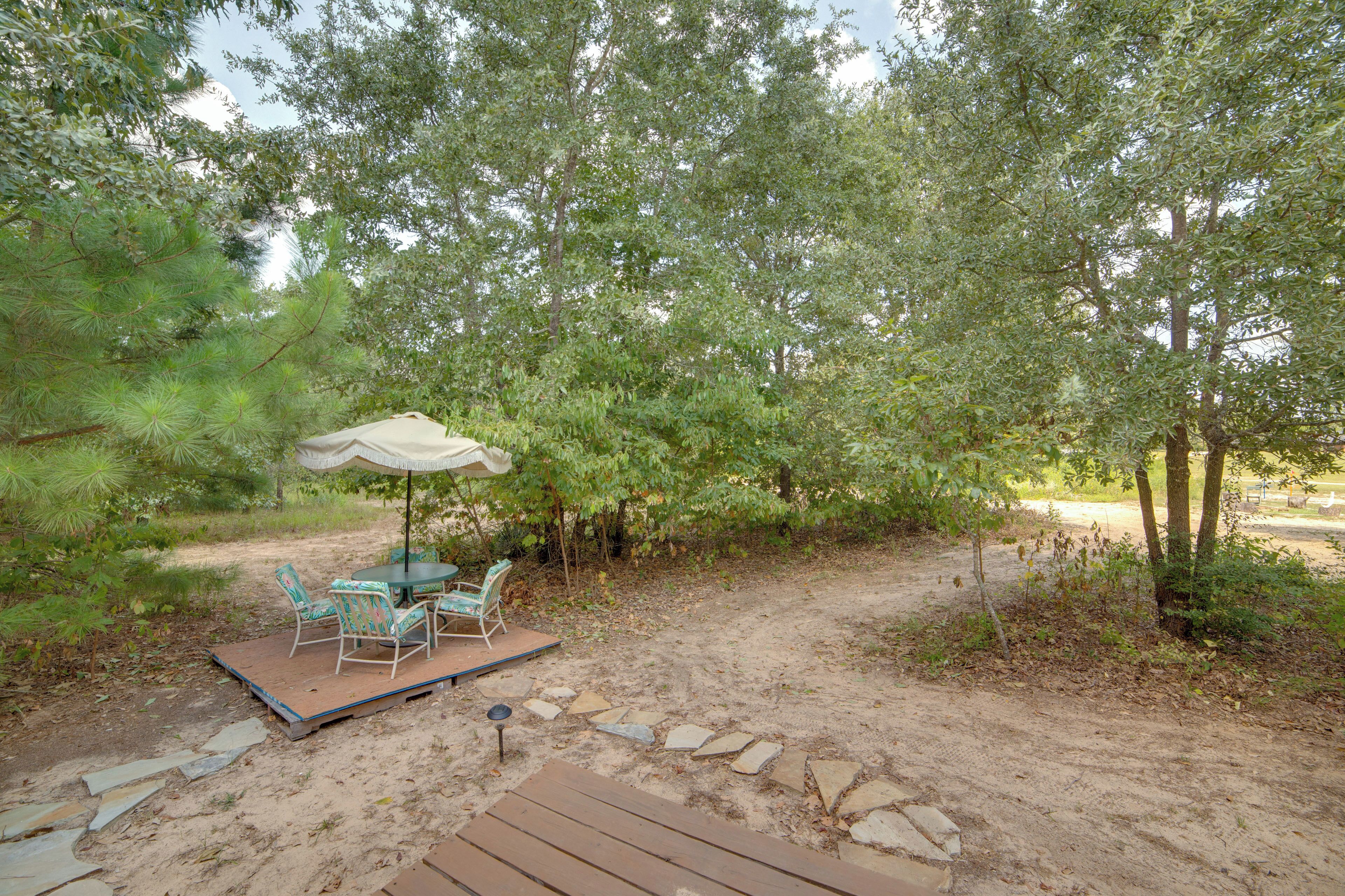 A patio with a table and chairs, surrounded by trees and a stone pathway.