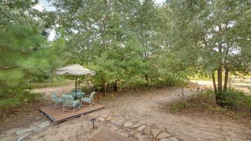 A patio with a table and chairs, surrounded by trees and a stone pathway.