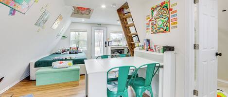 A room with a white desk, green chairs, a loft bed, and a ladder.