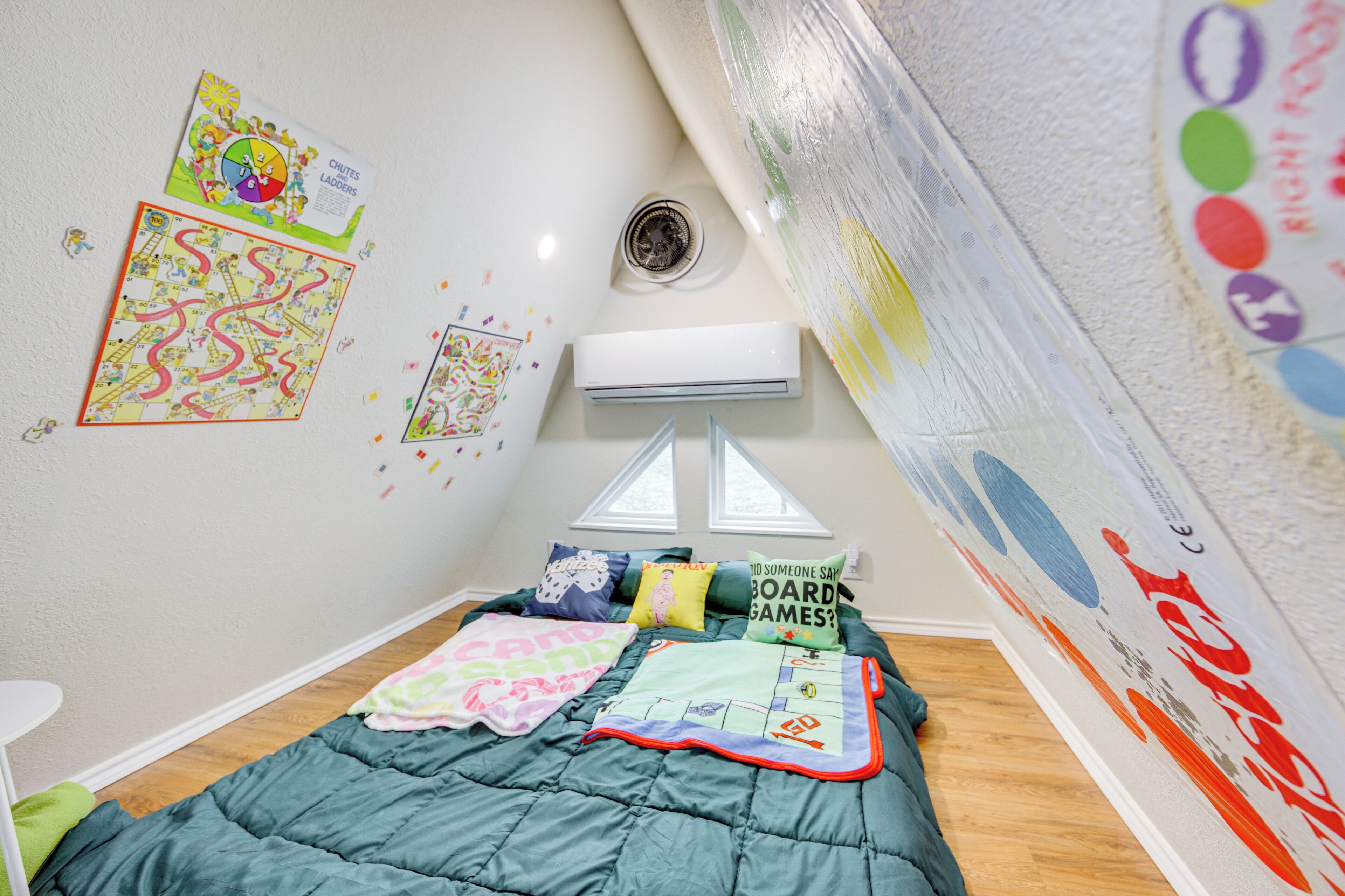 A bedroom with a bed, a window, and wall decorations including a game board and a poster.
