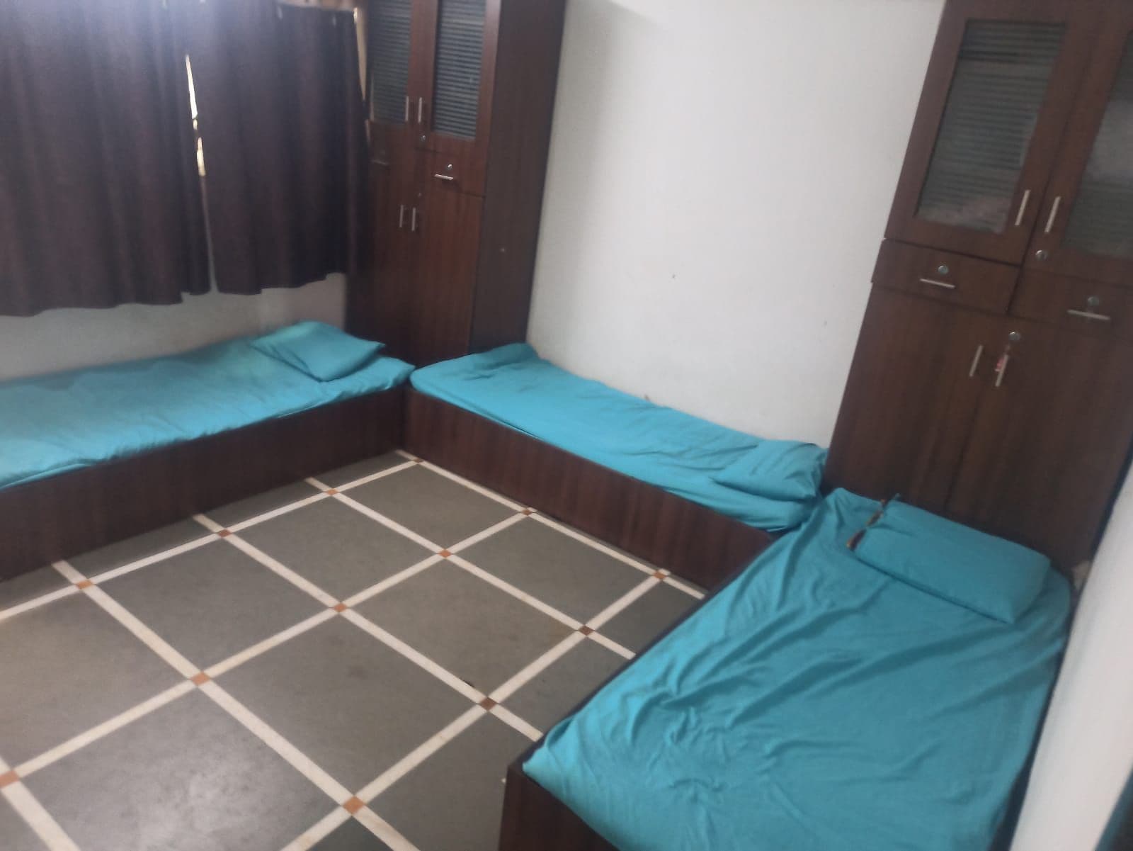 A small room with two single beds, a wardrobe, and a tiled floor.