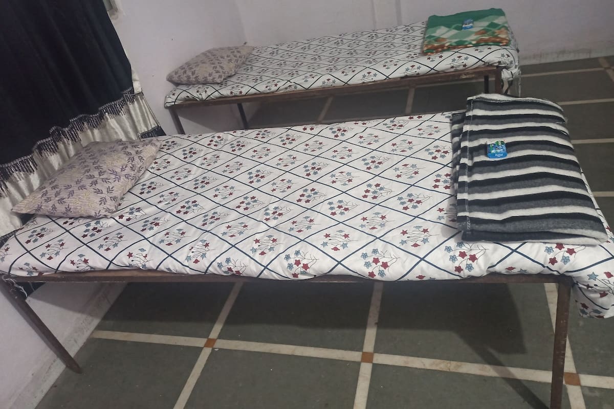 Dos camas individuales con ropa de cama estampada, una manta verde y una manta a rayas en el suelo.
