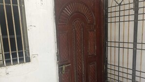 Une porte en bois fermée, surmontée d’un portail en métal, avec une fenêtre grillagée et un sol carrelé.