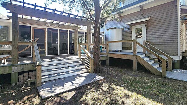 A wooden deck with a pergola, a staircase leading to a deck, and a house with a visible door and windows.