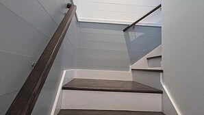 A staircase with wooden steps and white walls, leading to a landing with a small window.