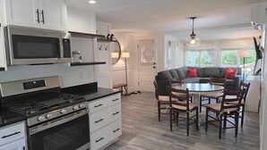 A modern kitchen with stainless steel appliances, a dining area with a round table and chairs, and a built-in seating area with a gray sofa and red cushions.