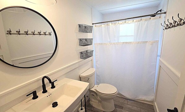 A bathroom with a white sink, a toilet, a round mirror, and a shower curtain.