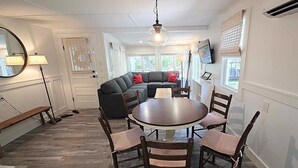 A dining area with a round table and four chairs, a black sofa with red cushions, and a large mirror on the wall.
