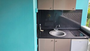 A compact kitchen with a sink, stove, and cabinets, set against teal walls. - L'ECRIN BLEU SEA VIEW DIAMOND ROCK (LE DIAMANT)