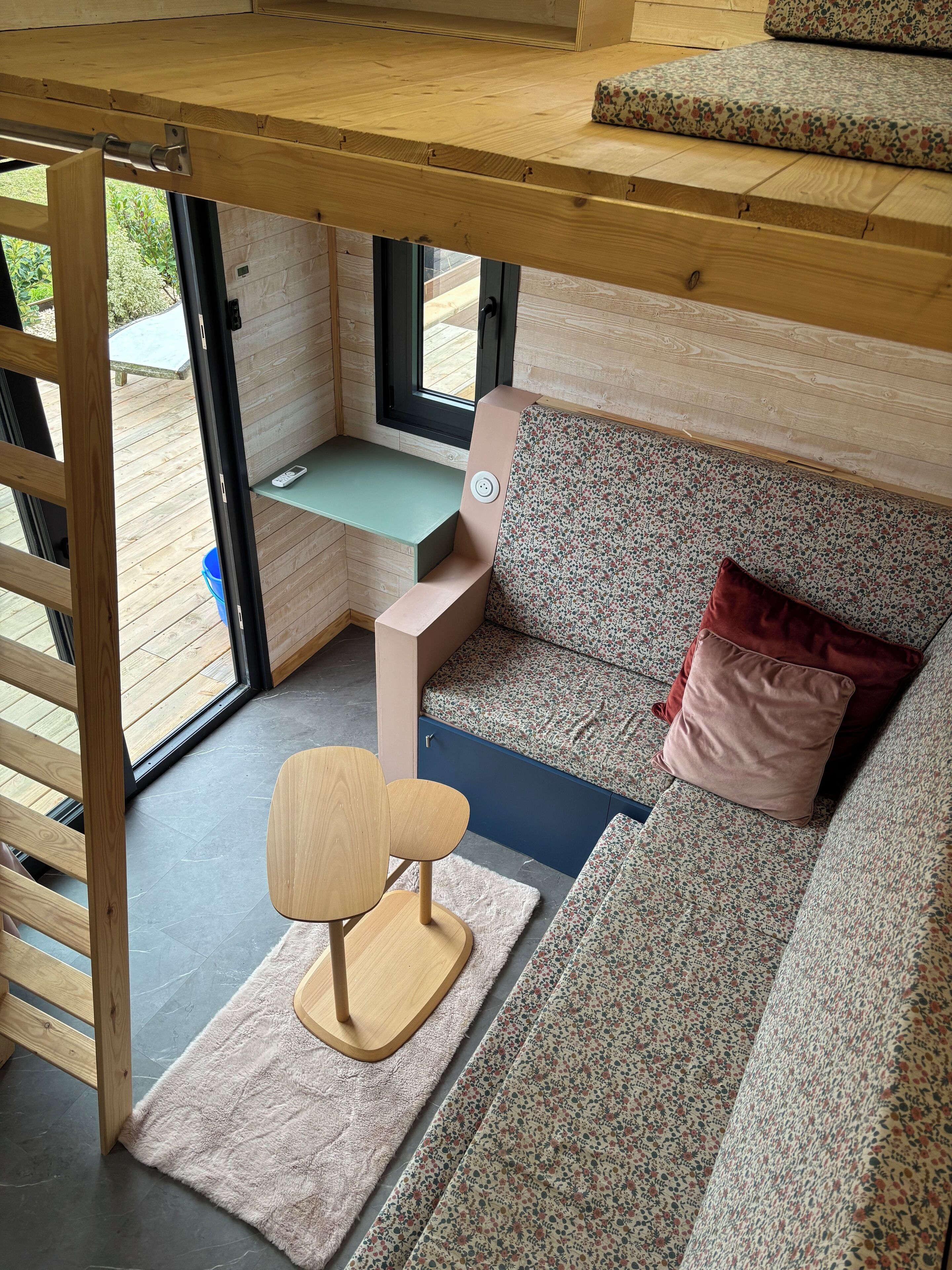 Een gezellige kamer met een houten plafond, een bank met bloemenstoffering, een roze kussen en een klein houten tafeltje.