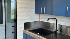A modern kitchen with dark blue cabinets, a black sink, and a wooden countertop. - Comfortable Tiny House in Saulges in the heart of nature. (Saulges)