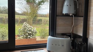 A kitchen with a built-in oven, a coffee maker, and a window with a view of a tree and garden. - Comfortable Tiny House in Saulges in the heart of nature. (Saulges)