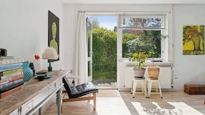 A bright room with a wooden desk, books, a chair, and a view of greenery outside. - Furnished Home by Sea & Fjords - Perfect for Remote Work Coastal Artist's Haven (Hundested)