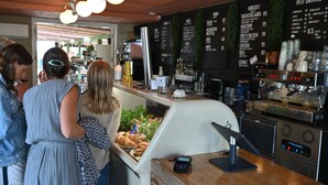 A café with a menu board listing items like burgers, hot drinks, and ice. There is a cash register and a digital display. - Furnished Home by Sea & Fjords - Perfect for Remote Work Coastal Artist's Haven (Hundested)