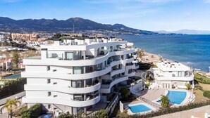 Un immeuble moderne à plusieurs étages, doté de balcons, d’une piscine et offrant une vue sur la mer et les montagnes.