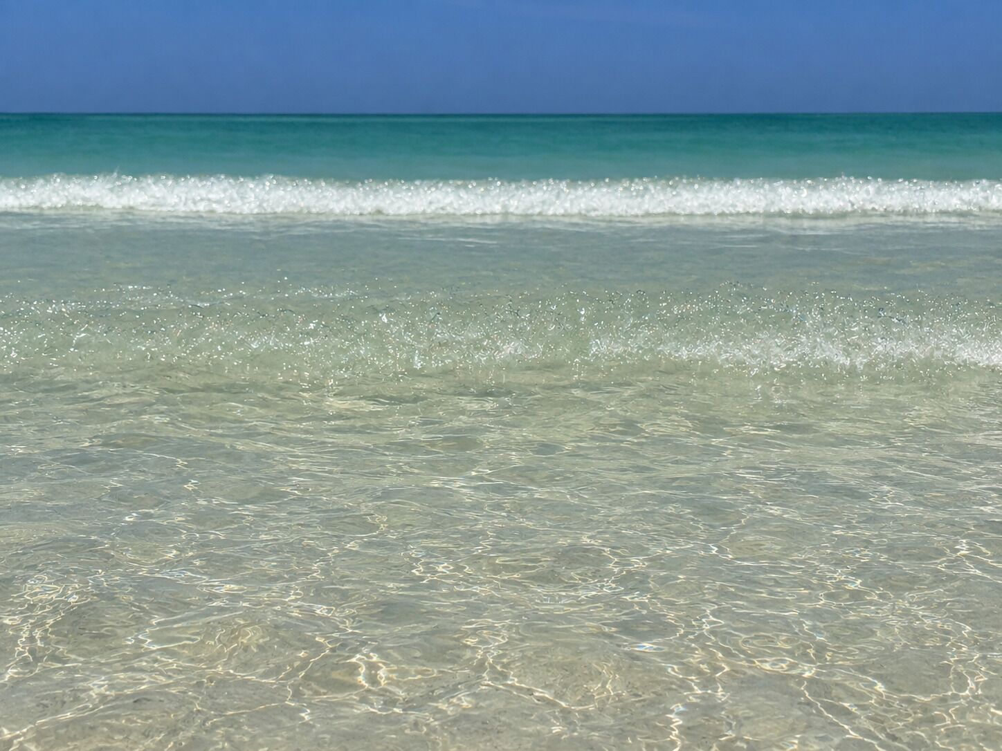 A beach with clear shallow water and gentle waves.