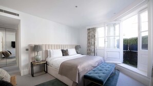 A bedroom with a large bed, bedside tables, a bench, and a window with curtains.