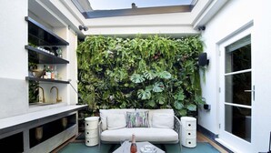 A cozy outdoor seating area with a white sofa, two side tables, and a glass-top table with a bottle and glasses.